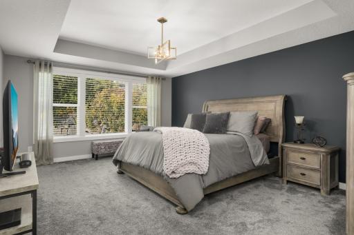 Spacious primary bedroom features a tray ceiling, large windows, plush carpeting, and an accent wall.