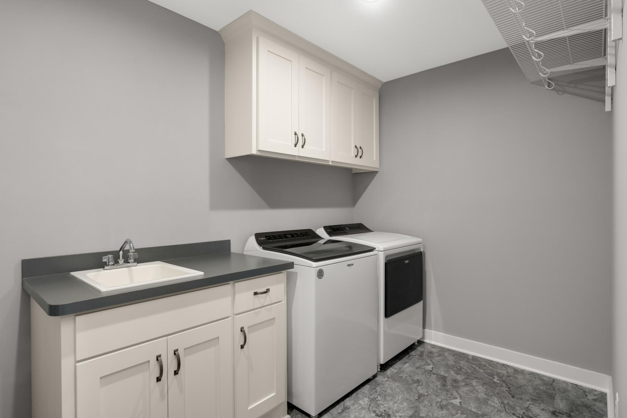 Convenient upper-level laundry room includes cabinetry, utility sink, counter space, and hanging storage.