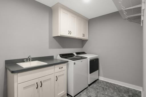 Convenient upper-level laundry room includes cabinetry, utility sink, counter space, and hanging storage.