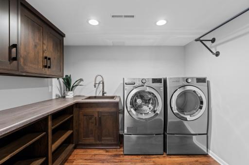 Thoughtfully designed laundry room with cabinets, sink and rail.