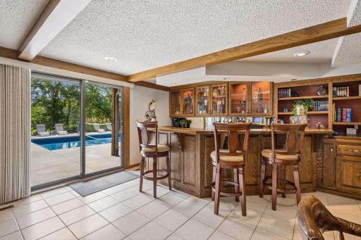 The walkout level family room is a natural gathering place and features a fun wet bar with lighted feature cabinets and plentiful shelving and built-ins for storage and display. Sliding doors open to the pool deck - perfect for entertaining!