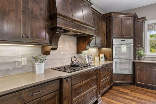 Warm & refined kitchen showcases rich walnut finished custom cabinetry, gas range, double ovens & beautifully crafted wood hood.