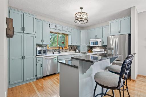 Updated kitchen with abundant cabinetry, stainless steel appliances, tile backsplash, and a large center island with seating.
