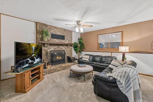 The cozy lower-level family room offers the perfect place to relax and unwind, featuring a charming wood-burning fireplace with a raised hearth and an impressive full-wall brick surround