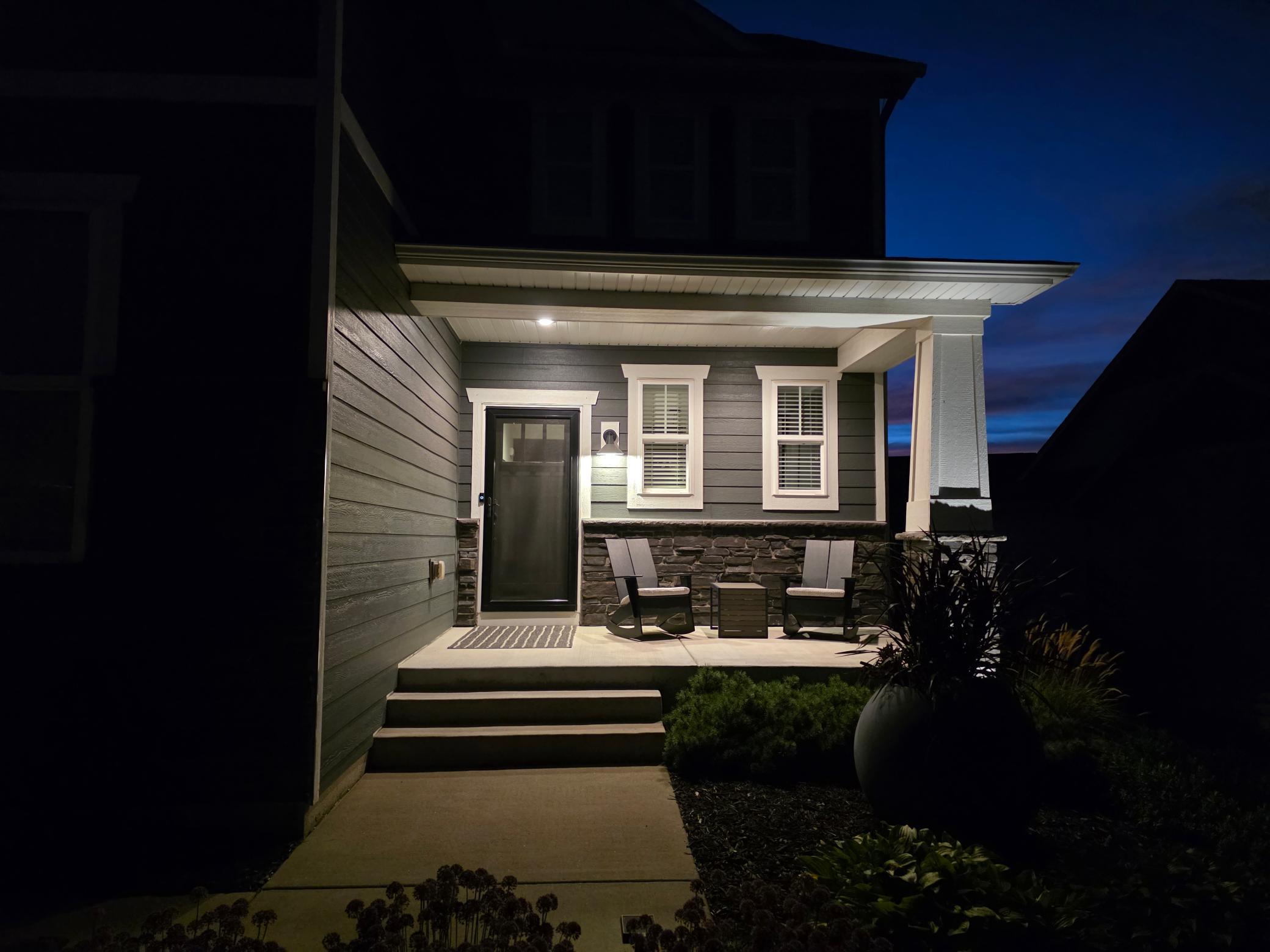 Covered concrete front porch creates an inviting arrival with stone accents and illuminated landscaping.