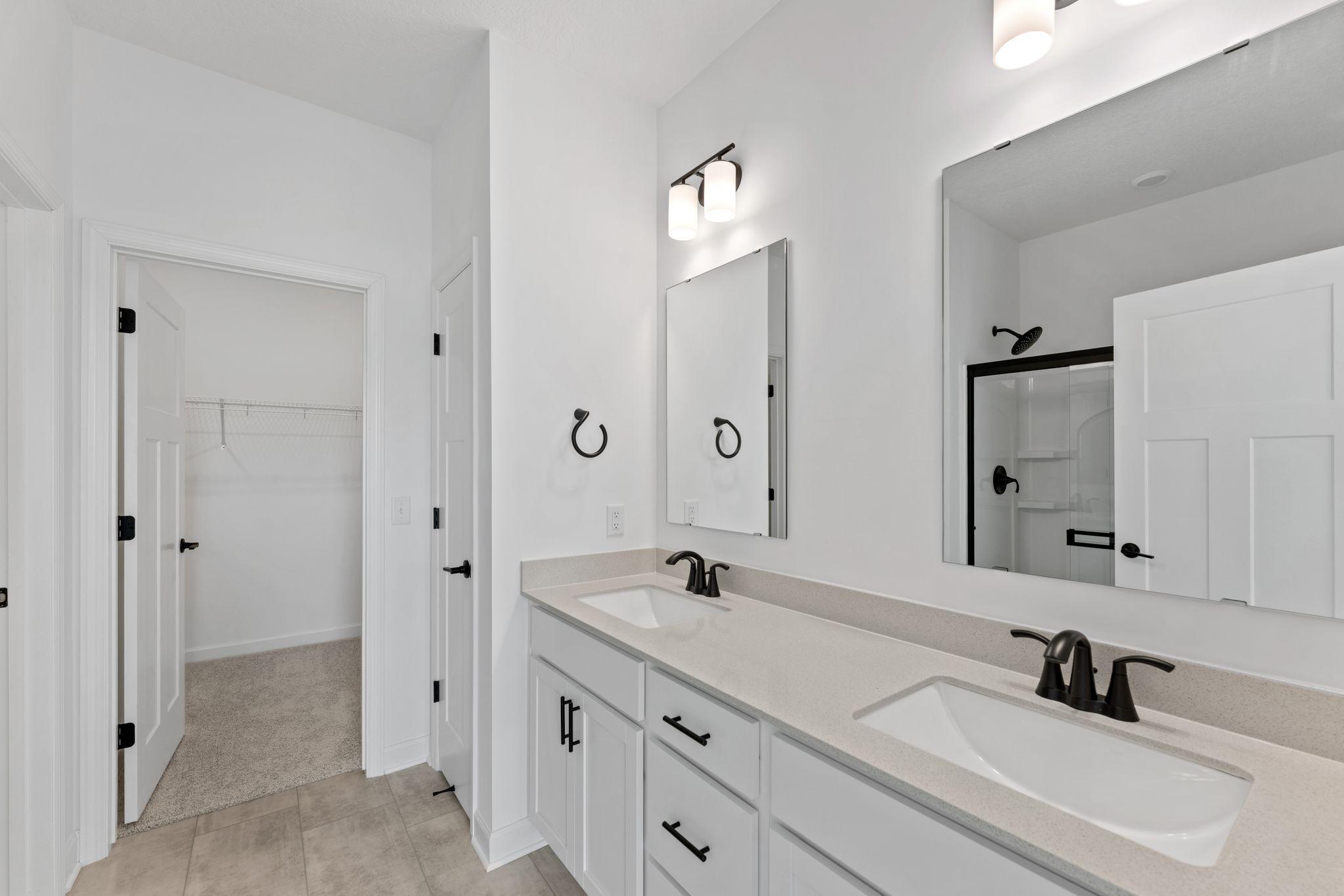 Quartz-topped dual undermount sinks with Moen® faucets in the spa-inspired owner’s suite bathroom