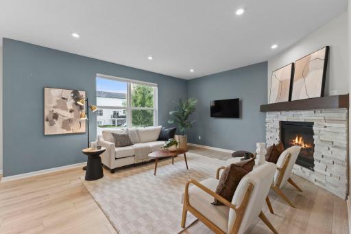 Spacious living room filled with natural light from oversized windows. A beautiful stone fireplace creates the perfect focal point for the space.