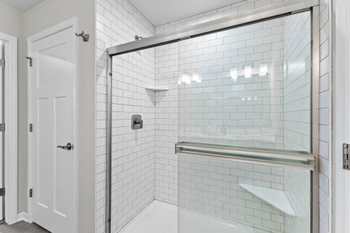 The primary bath is upgraded with a beautifully tiled walk-in shower featuring a glass enclosure and built-in corner shelving.
