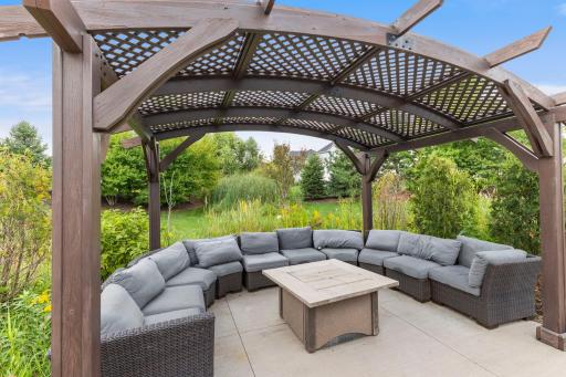 Pergola-covered gathering area with bar-height seating and plenty of room to relax outdoors, surrounded by beautiful landscaping.