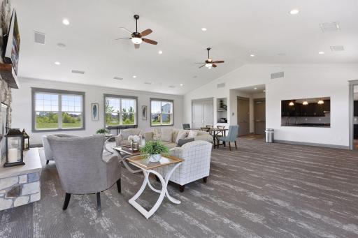 Another view of the impressive community gathering space, featuring comfortable lounge seating, large windows, a stone fireplace, and convenient access to the community kitchen.