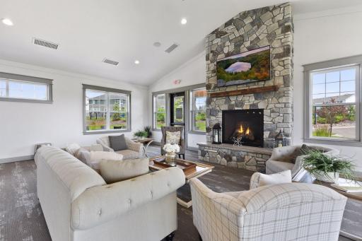 Beautiful community gathering room featuring a dramatic stone fireplace, comfortable seating, abundant natural light, and a warm, welcoming atmosphere.