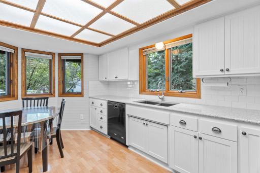 The updated kitchen features newer countertops, subway tiled backsplash, white cabinetry, stylish fixtures, and wainscoting accents. Kitchen windows create a sun-filled, open space.