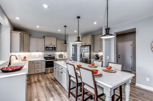 A bright and luxurious kitchen is the centerpiece of this home with stainless appliances, quartz countertops and lots of natural light while stylish pendant lights add a modern refined touch. (model photo)