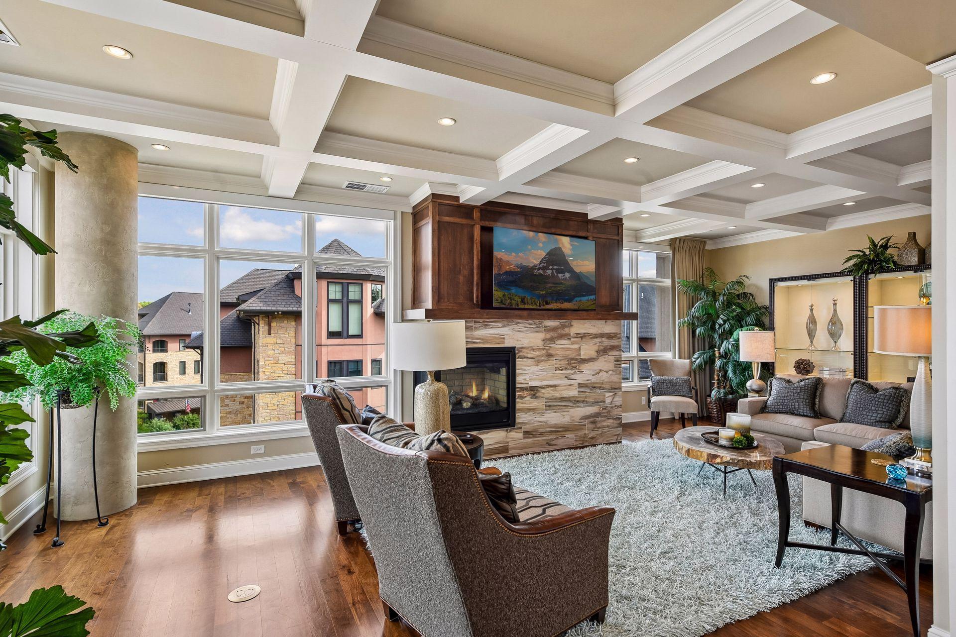 Gather and entertain in this spacious living room, featuring a striking gas fireplace, detailed coffered ceiling, expansive windows, and ample seating.