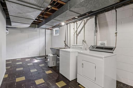 Half of the lower level remains unfinished, housing the laundry area with a classic concrete utility sink and flexible space for storage or future projects