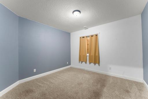 Inviting third lower-level flexible room for a bedroom, office or hobby space featuring an egress window, offering comfort, natural light, and added functionality.