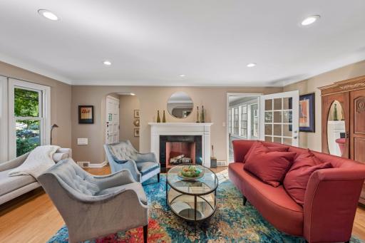 Living Room - Spacious main-level living room centers around a classic fireplace with white mantel, complemented by hardwood floors, recessed lighting, and large windows.