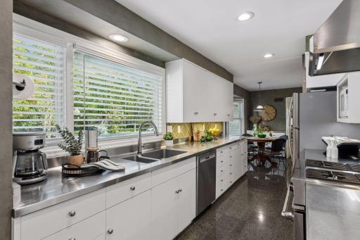 Kitchen - Bright galley-style kitchen features extensive white cabinetry, stainless counters, large windows, recessed lighting, dishwasher, gas range, and an adjoining dining nook.
