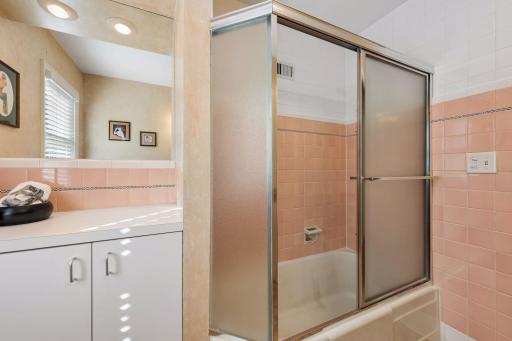 Full Bathroom - A closer look at the tub/shower highlights the bathroom's classic pink and white tilework, glass enclosure, and additional built-in storage.