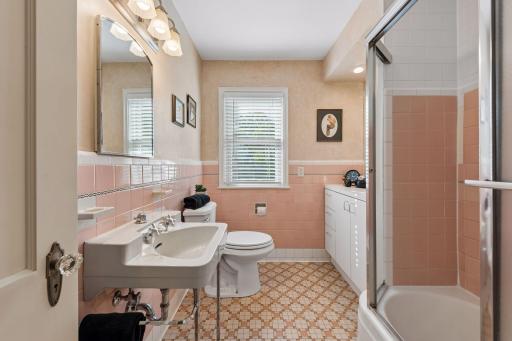 Full Main Floor Bathroom - Vintage character shines in this full bath with classic pink tile, mosaic tile flooring, pedestal sink, additional cabinetry, and a tub/shower.