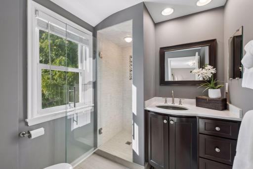 Primary Bathroom - Updated primary bath features a glass-enclosed tiled shower, dark wood vanity with light countertop, recessed lighting, and natural light from the window.