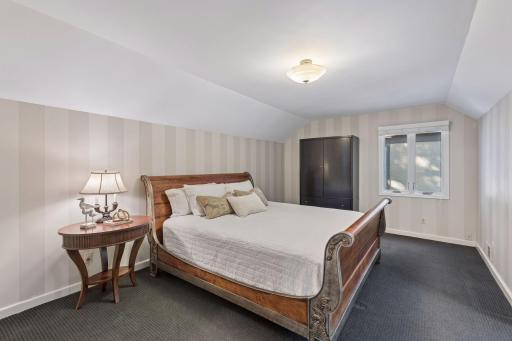 Upper-Level Bedroom - Spacious upper bedroom features a distinctive sloped ceiling, neutral paint striped walls, and room for a large bed and additional furniture.