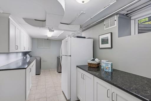 Laundry Room - Well-organized lower-level laundry area offers extensive cabinetry, long countertops, tile flooring, utility sink, and space for an additional refrigerator.