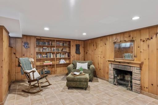 Lower-Level Fireplace - A closer view highlights the brick fireplace, built-in bookshelves, knotty-pine walls, and dedicated sitting area in the lower-level family room.