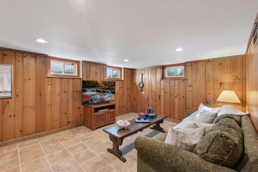 Lower-Level Family Room - Another view highlights the spacious lower-level family room with knotty-pine walls, tile flooring, recessed lighting, and multiple windows bringing in natural light.