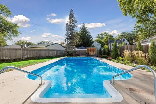 In-Ground Pool - A view from the pool steps highlights the poolâs generous size, surrounding concrete deck, mature landscaping, and privacy fencing.