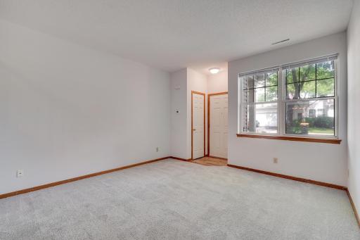 A view of the same space which features high ceilings, big and bright front windows and new carpeting.