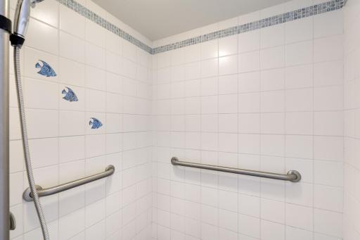 Tiled walk-in shower with grab bars and a handheld showerhead for added functionality and convenience.
