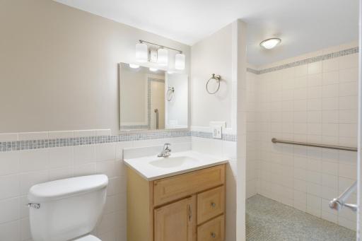 Bright bathroom featuring a wood vanity, tiled walls, and a spacious walk-in shower.