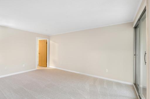 Another view of the spacious primary bedroom showcasing its generous proportions, neutral finishes, and convenient access to the adjoining balcony.