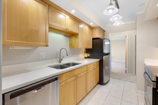 Well-appointed kitchen featuring warm wood cabinetry, generous counter space, a double-basin sink, stainless steel dishwasher, and overhead lighting for a bright, functional workspace.