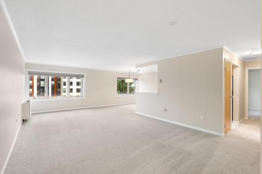 Spacious living room with fresh neutral carpet, crown molding and large windows that fill the space with natural light.