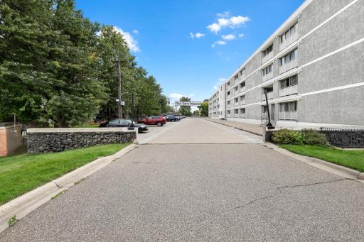 Private drive with additional parking alongside the building, framed by mature trees
