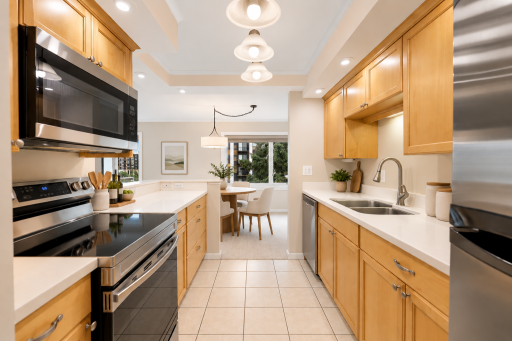 Virtually staged galley kitchen featuring warm wood cabinetry, generous counter space, stainless-steel appliances, and an adjoining dining area filled with natural light.