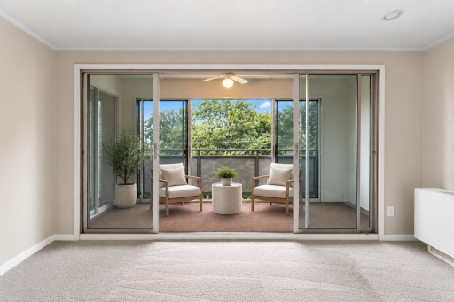 Virtually staged view highlighting the enclosed balcony/sunroom with floor-to-ceiling sliding glass doors, treetop views, and space for a cozy seating area.