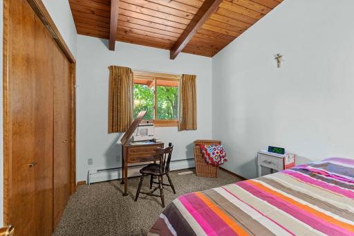 Main level bedroom 2 offers a vaulted wood ceiling, exposed beams, and space for a desk or study area