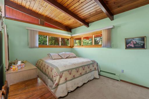 The main level primary bedroom is filled with natural light from wraparound windows and features beautiful wood ceilings and exposed beams overhead