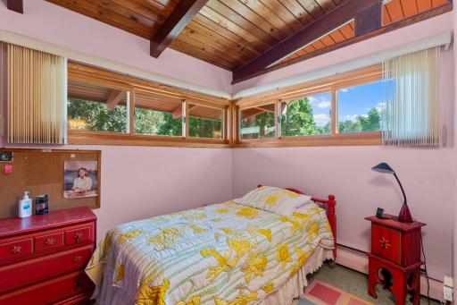 Main level bedroom 4 with wraparound windows making this room especially bright and inviting while offering lovely views of the surrounding trees