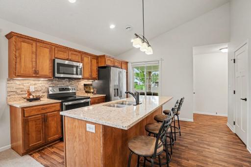 The bright kitchen features stainless-steel appliances, granite counters, a glass mosaic backsplash, under cabinet lighting, pendant lights, recessed lights and a large window.