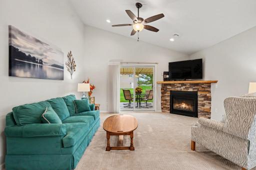 The living room includes a 12' vaulted ceiling, a corner gas fireplace with stacked stone surround, a ceiling fan, recessed lights, knockdown ceiling and a walk-out patio door to the stamped concrete patio out back.
