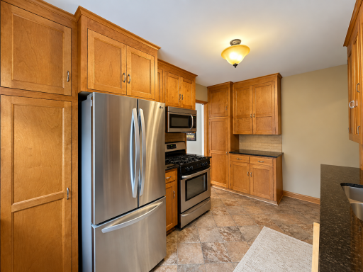 Tall wood cabinets provide substantial storage for groceries and cookware, with more cabinets and counter space across the kitchen. A gas range and stainless steel appliances complete the setup.