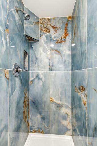 This gorgeous walk-in shower makes a bold statement with floor-to-ceiling blue and gold marble-look tile, polished fixtures, and two built-in niches for convenient storage.