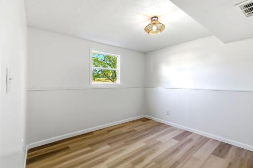 The second bedroom offers fresh paint, new flooring, natural light, and a unique ceiling design accented by a stylish modern light fixture. Its flexible layout makes it ideal as a comfortable bedroom, nursery, or home office.