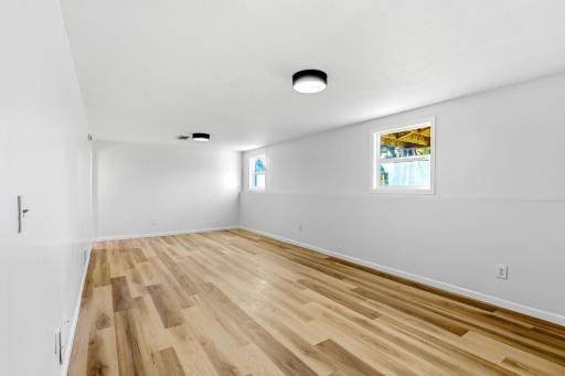 This additional view highlights the impressive size of the lower-level family room, with plenty of space to create separate areas for relaxing, entertaining, playing, or working from home. Multiple windows, new flooring, and modern lighting keep the