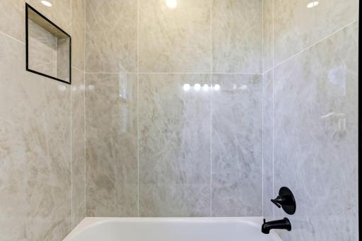 Relax in the full-size bathtub surrounded by elegant, large-format stone-look tile extending to the ceiling. Contemporary matte-black fixtures, an oversized rainfall-style showerhead, and a built-in niche complete the clean, spa-inspired design.