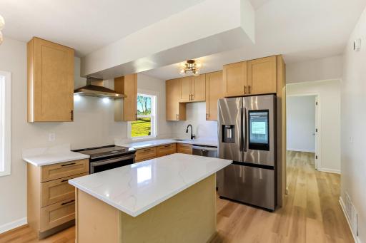 Beautifully renovated open-concept kitchen featuring a large center island, granite countertops, new stainless-steel appliances, modern cabinetry, and new flooring that continues throughout the home, perfect for cooking, gathering, and entertaining.